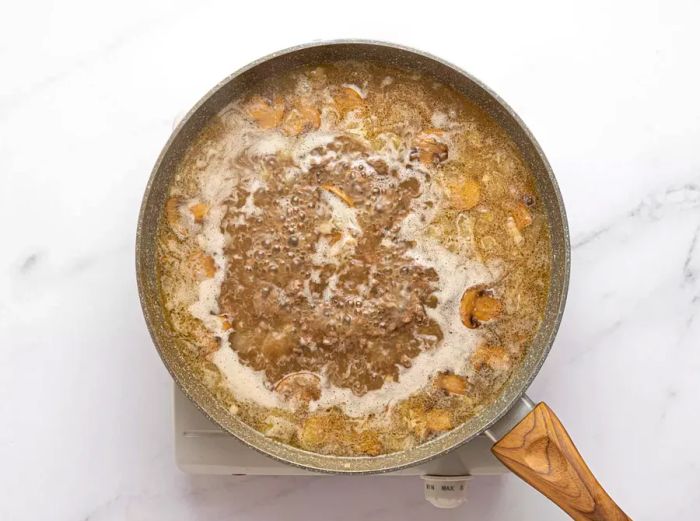 Ground beef and sliced mushrooms simmering in broth in a skillet.