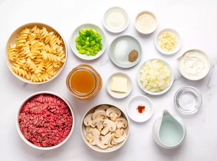 An assortment of white bowls filled with the ingredients for ground beef stroganoff.