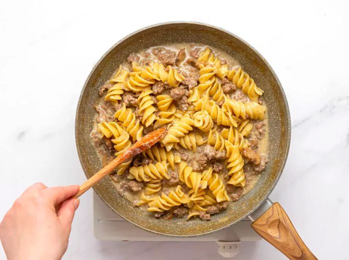 A person stirring the ground beef stroganoff mixture in a skillet.