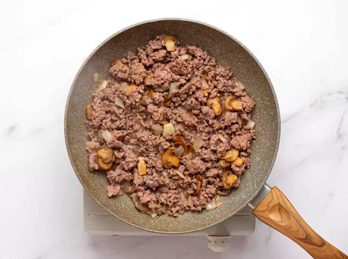 Ground beef and sliced mushrooms sautéing in a skillet.