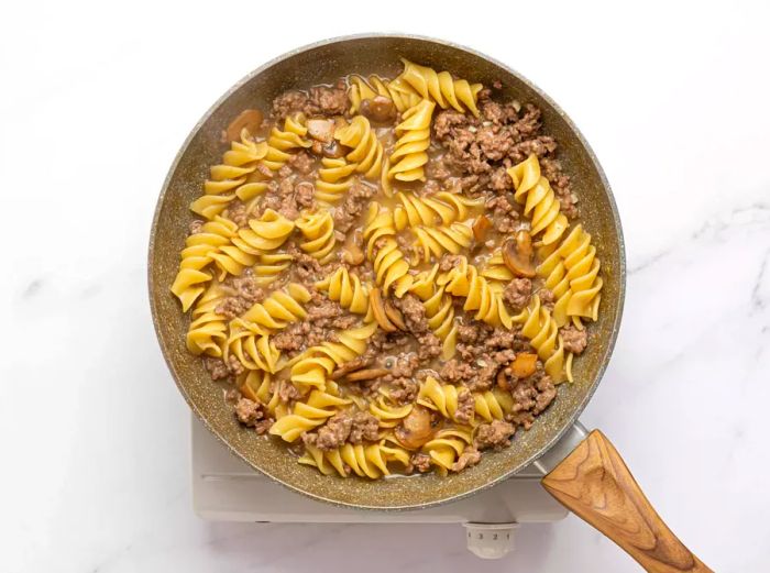 Rotini noodles cooking in a ground beef mixture in a skillet.