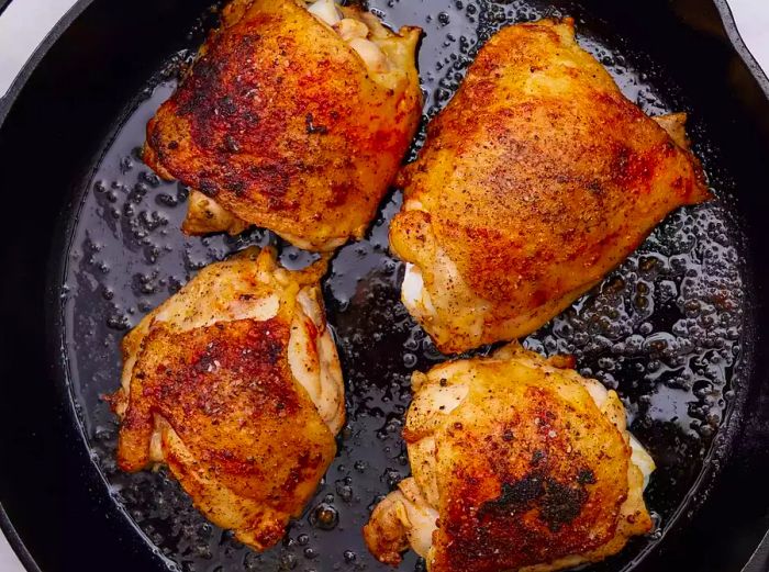 A cast iron skillet containing baked, golden-brown chicken thighs.