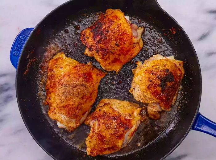 A cast iron skillet containing four golden-brown chicken thighs.