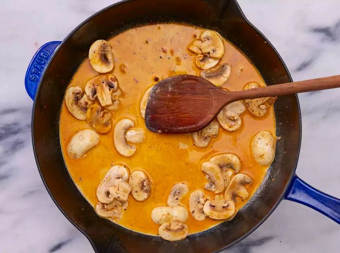 A cast iron skillet with sliced mushrooms simmering in a creamy sauce.