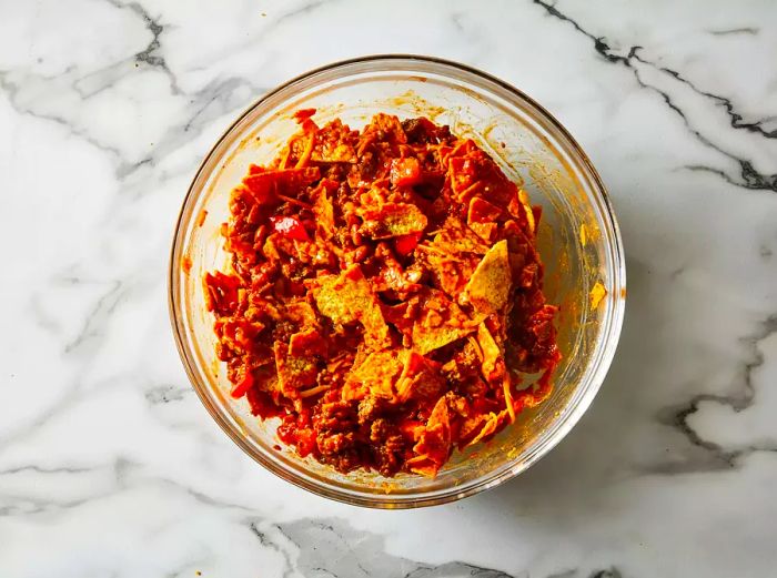 A top-down view of taco salad ingredients mixed together in a glass bowl.