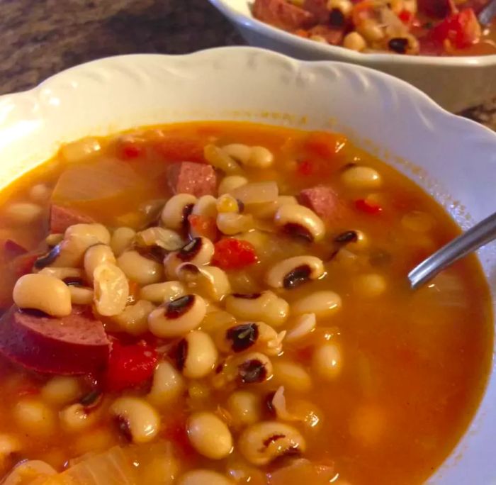 A bowl of black-eyed peas with ham, accompanied by a spoon