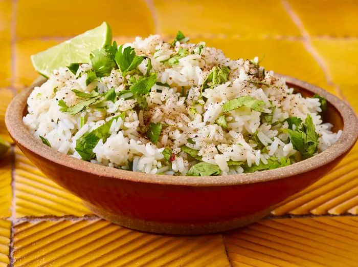 A mid-low angle shot of a heaping bowl of cilantro lime rice, topped with a lime wedge.