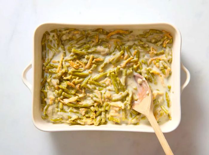 A casserole dish filled with green beans mixed with creamy mushroom soup, milk, and topped with crunchy fried onions.