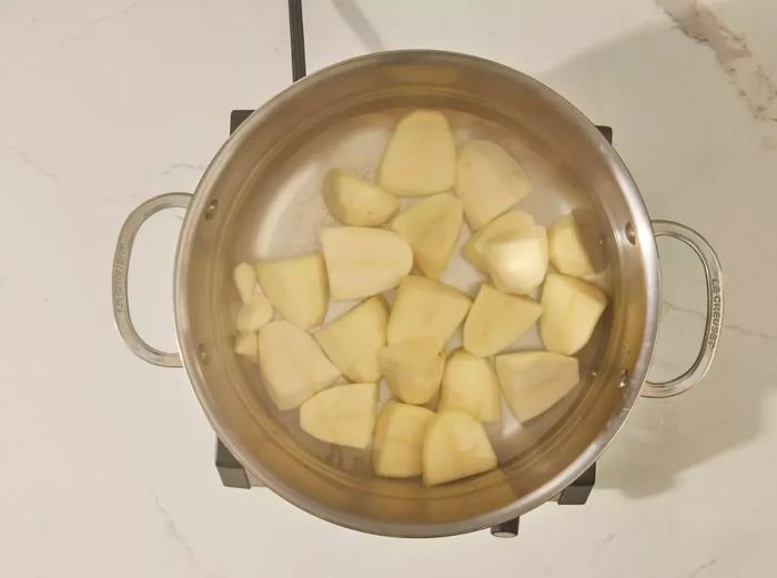 A large pot with peeled potatoes and garlic submerged in water