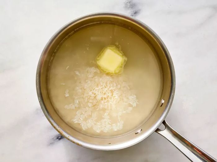 Butter and rice mixed into boiling water in a saucepan.