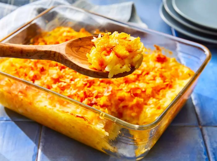 A baking dish of Simply Potatoes cheesy hash browns, with a wooden spoon serving a scoop