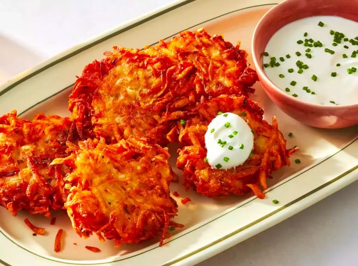 Potato pancakes served on a platter, accompanied by a bowl of sour cream topped with fresh chives on the side.