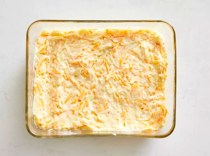 A glass baking dish filled with a cheesy potato mixture