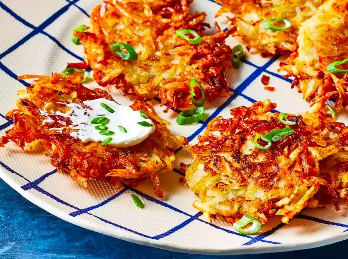 a plate of crispy potato pancakes, garnished with sour cream and sliced green onions