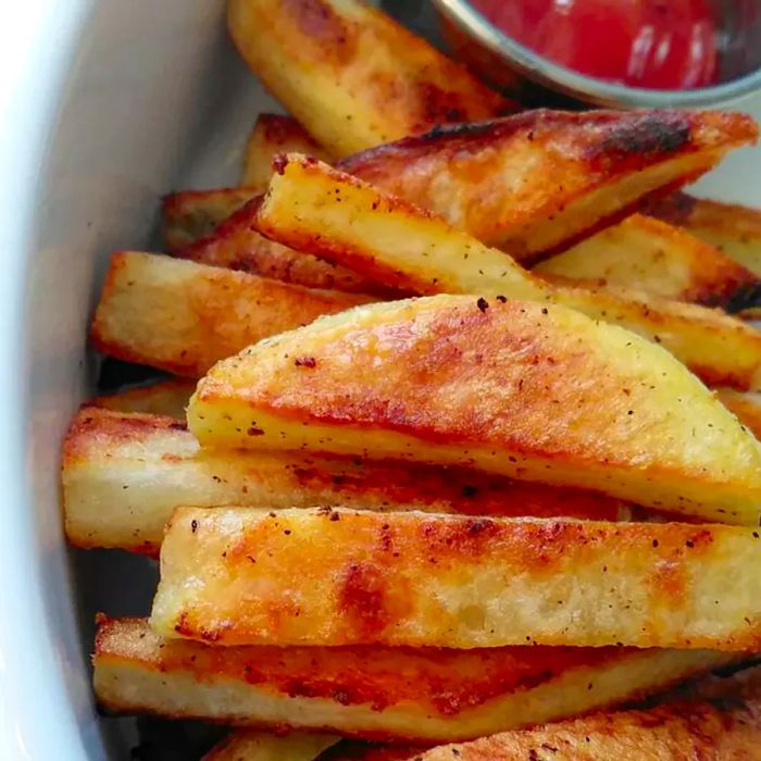 A close-up shot of crispy baked French fries served in a white bowl with a side of ketchup in a small bowl.