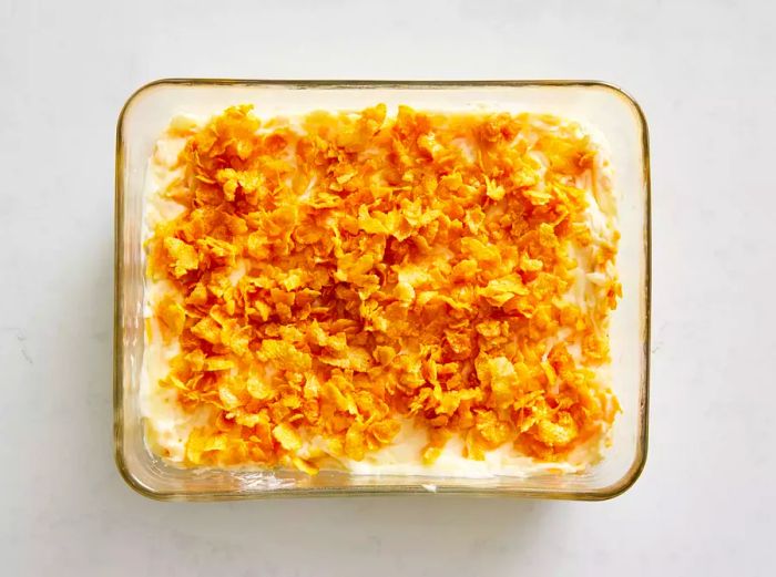 A glass baking dish filled with cheesy potato mixture, topped with buttery cornflakes