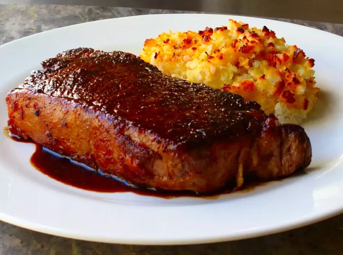 A plate of Chef John’s Steakhouse Potatoes Romanoff served alongside a perfectly cooked steak.