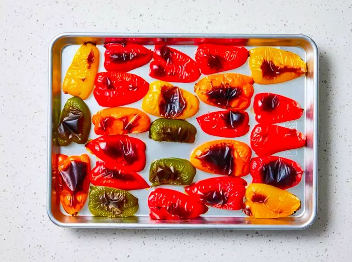 A sheet pan filled with blistered, quartered bell peppers, showing blackened areas of skin