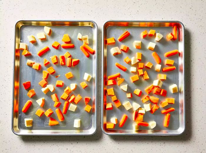 The yams, parsnips, and carrots are spread evenly across the two baking sheets.