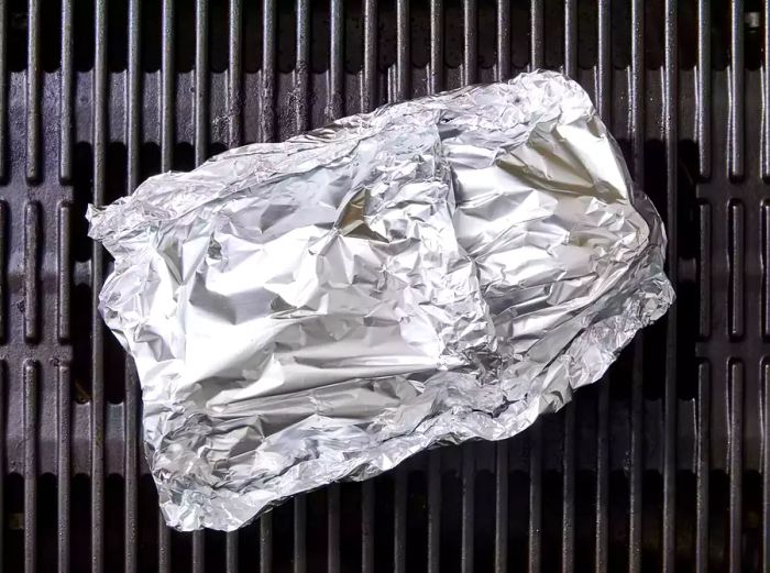 A tightly sealed foil packet of beets resting on the grill grates