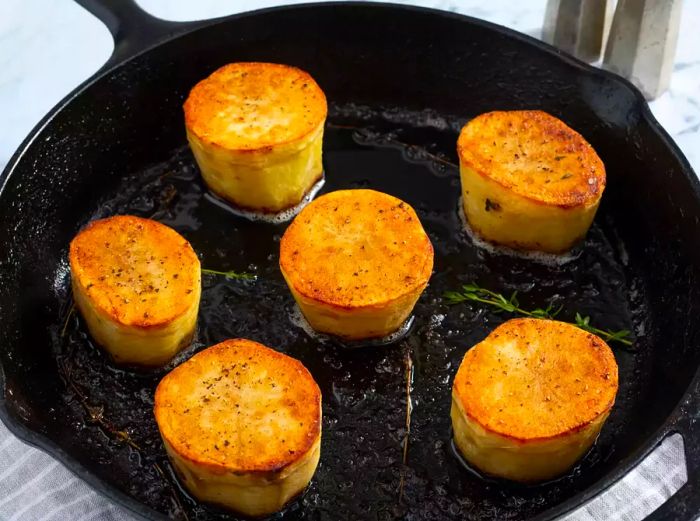 Overhead shot of fondant potatoes garnished with herbs in a skillet