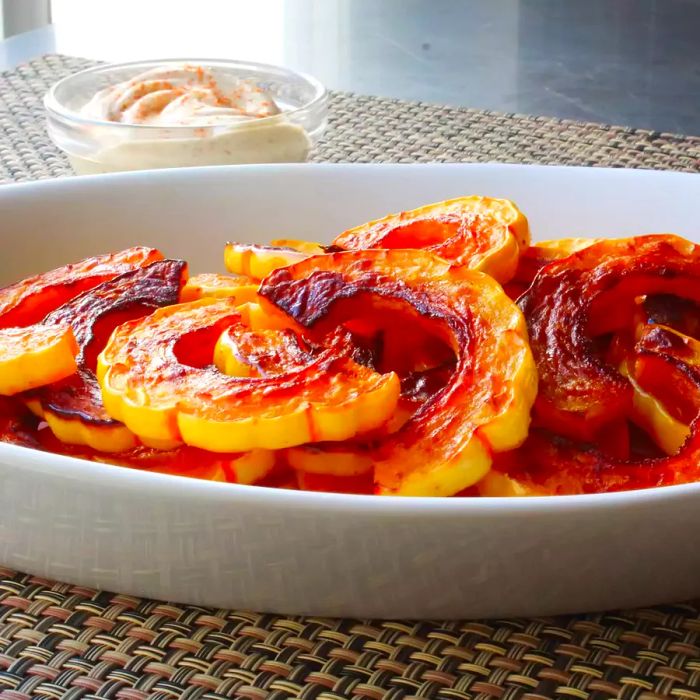 A close-up of Roasted Delicata Squash served on a white platter, with a dipping sauce in the background.