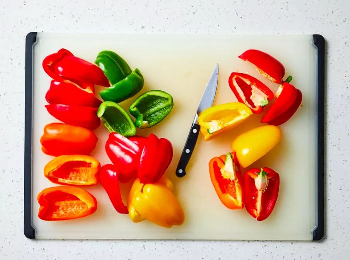 A cutting board with quarters of red, orange, yellow, and green bell peppers