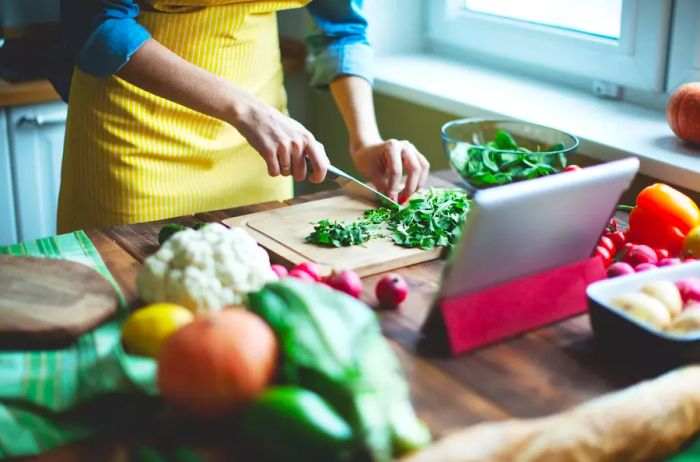 A woman chopping fresh vegetables on a cutting board.
