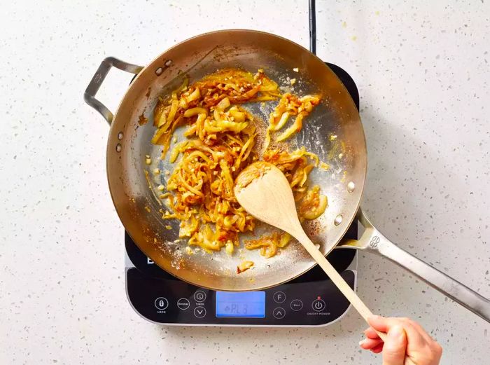A pan with caramelized onions, garlic, and flour being stirred together with a wooden spoon.