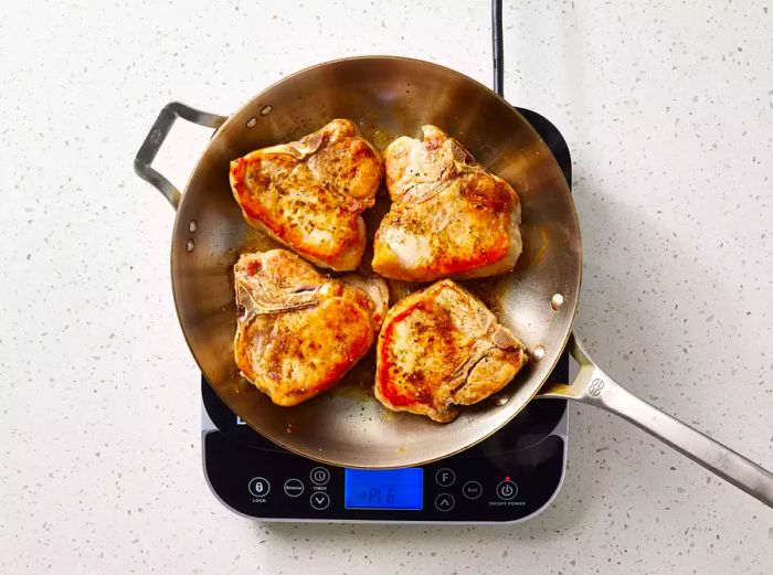 A skillet with four pork chops browned to perfection.