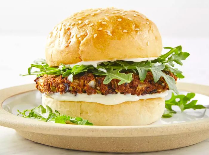 A low-angle shot of a black bean veggie burger on a bun with arugula, served on a beige plate.