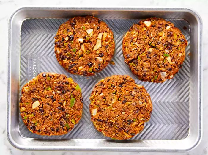 Four round veggie black bean patties arranged on a baking tray.