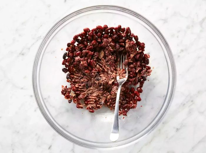 Black beans mashed with a fork in a transparent bowl.
