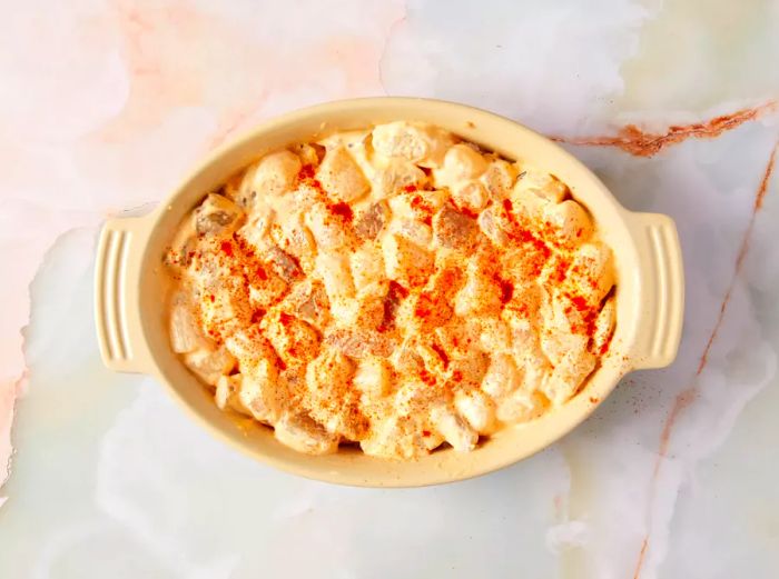 A casserole dish filled with shrimp and scallops, covered with a mayo mixture and seasonings.