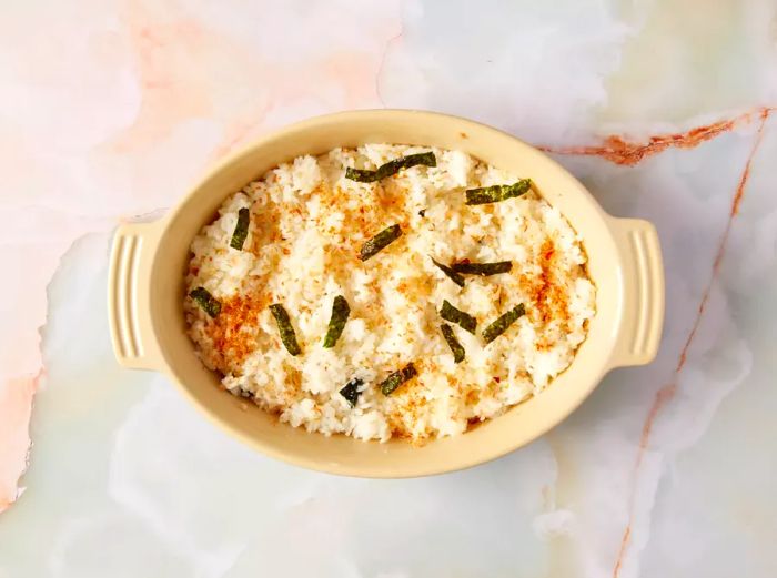 Cooked rice in an oval casserole dish, topped with seasonings.
