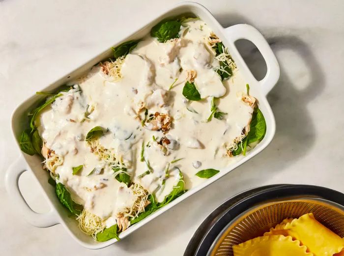 Chicken and Spinach Alfredo Lasagna topped with sauce in a baking dish