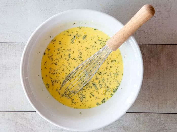 Whisked eggs, milk, and parsley blended together in a bowl