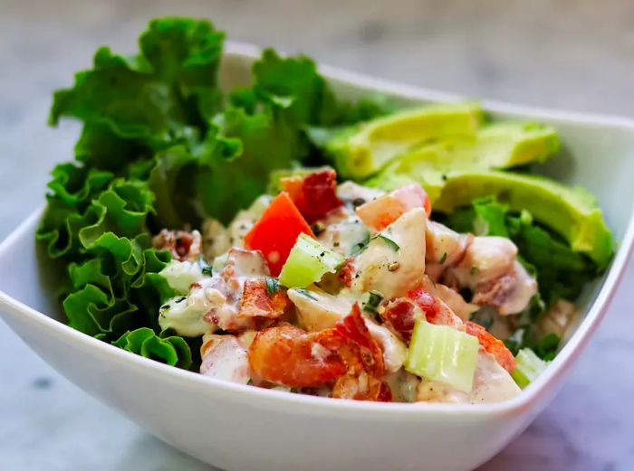 A close-up shot of a Chicken Salad with Bacon, Lettuce, Tomato, and Avocado served in a white bowl