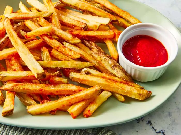 Close-up view of golden French fries on a plate served with a ramekin of ketchup
