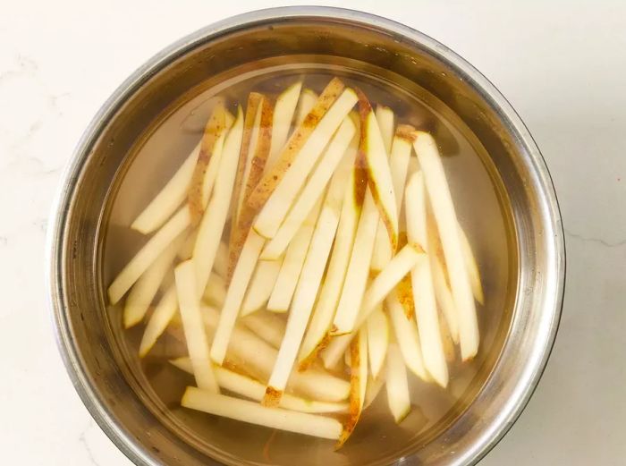 Aerial view of a bowl filled with sliced potato strips soaking in water