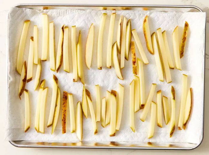Overhead shot of a baking sheet with potato fries laid out on paper towels