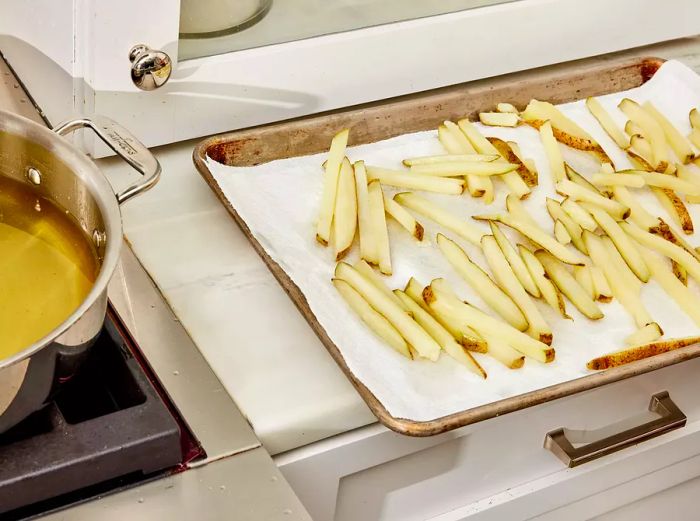 A high-angle view of partially cooked fries resting on a baking sheet lined with paper towels