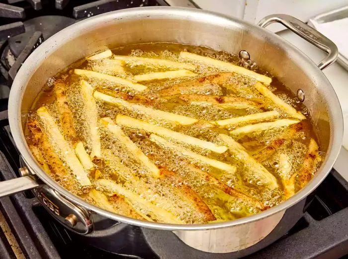 A high-angle view of cut potatoes frying in a pan of hot oil to make crispy fries