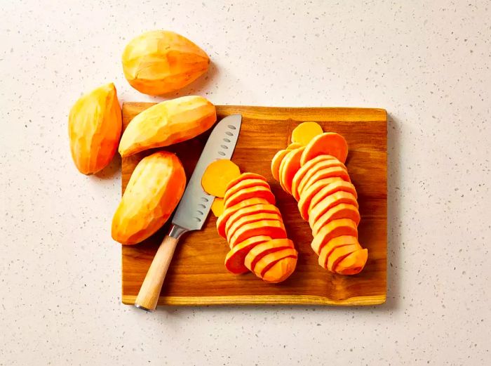 A cutting board with peeled and sliced sweet potatoes ready to cook.