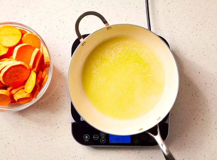 A spacious pan with melted butter, accompanied by a bowl of sliced sweet potatoes.