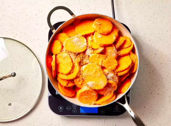 A large pan of sweet potato slices cooking in butter, topped with a cinnamon-sugar mixture.