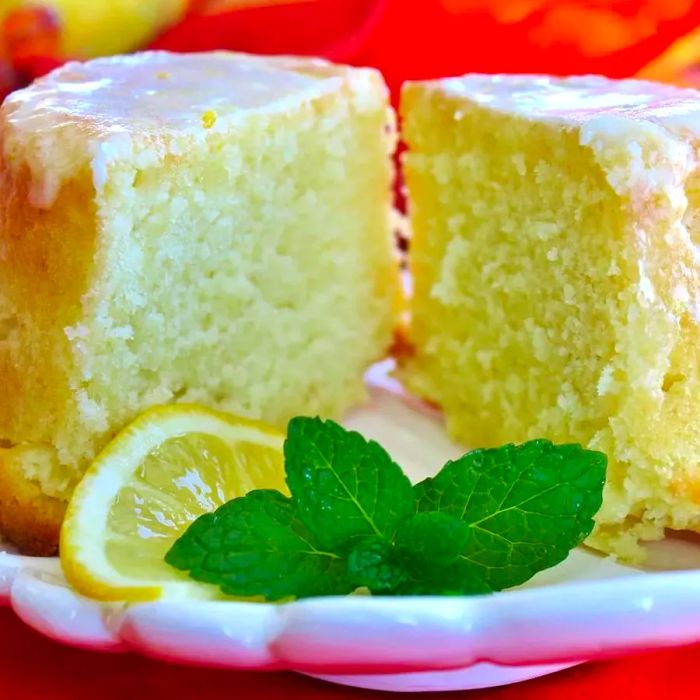 A slice of pound cake on a white plate, topped with a glaze, a lemon slice, and a mint garnish