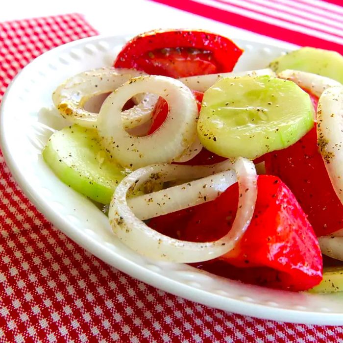 A white ceramic bowl filled with tomato wedges, cucumber slices, and onion rings