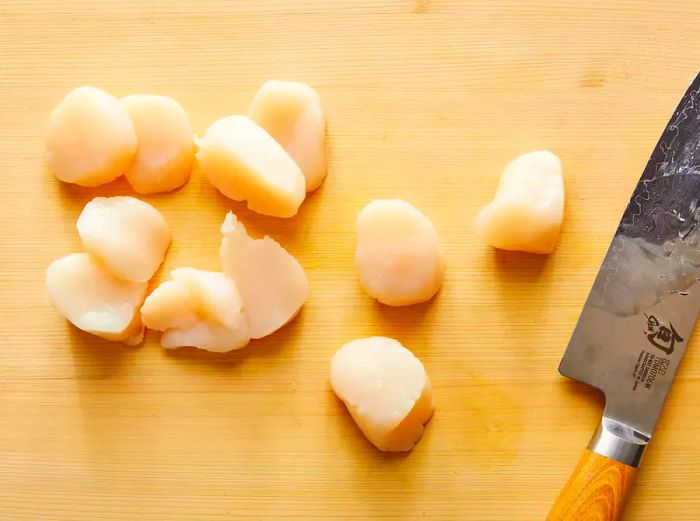 A top-down view of scallops being sliced in half to reduce thickness.