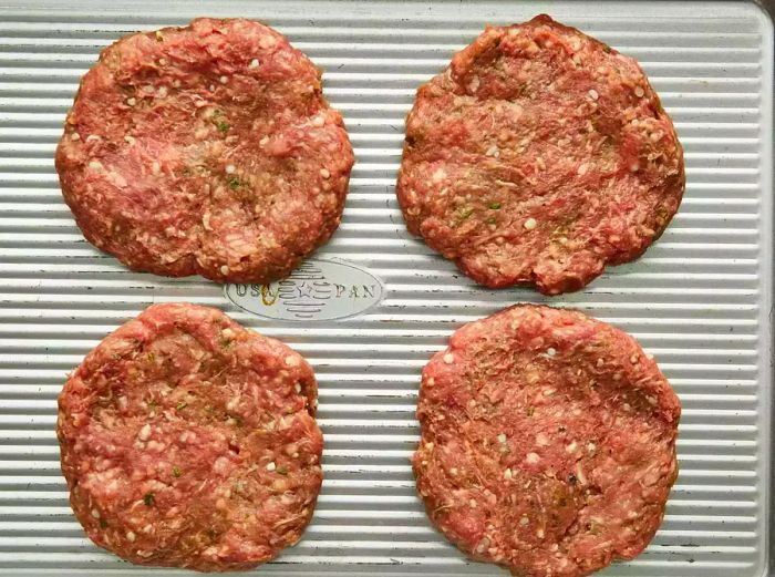 A top-down view of four lamb patties arranged on a baking sheet.
